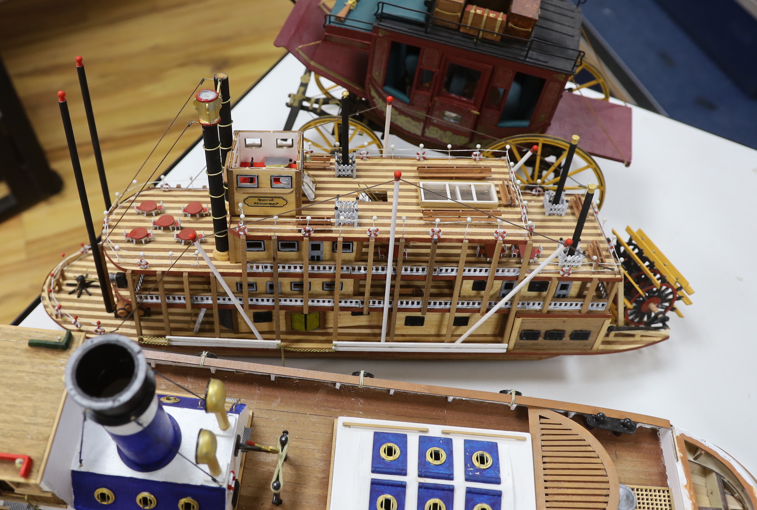 Two scratch built wooden model boats; a Mississippi style paddle steamer and a steam tug, together with a U.S. Western style coach plus a pocket watch and stand in the form of a long case clock, tug length 81cm